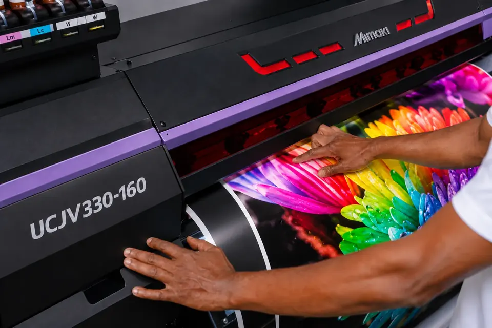 An operator’s hands guiding a multicoloured floral print on a Mimaki UCJV330-160